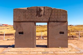 Ancient stone gateway with carved symbols under a clear blue sky.