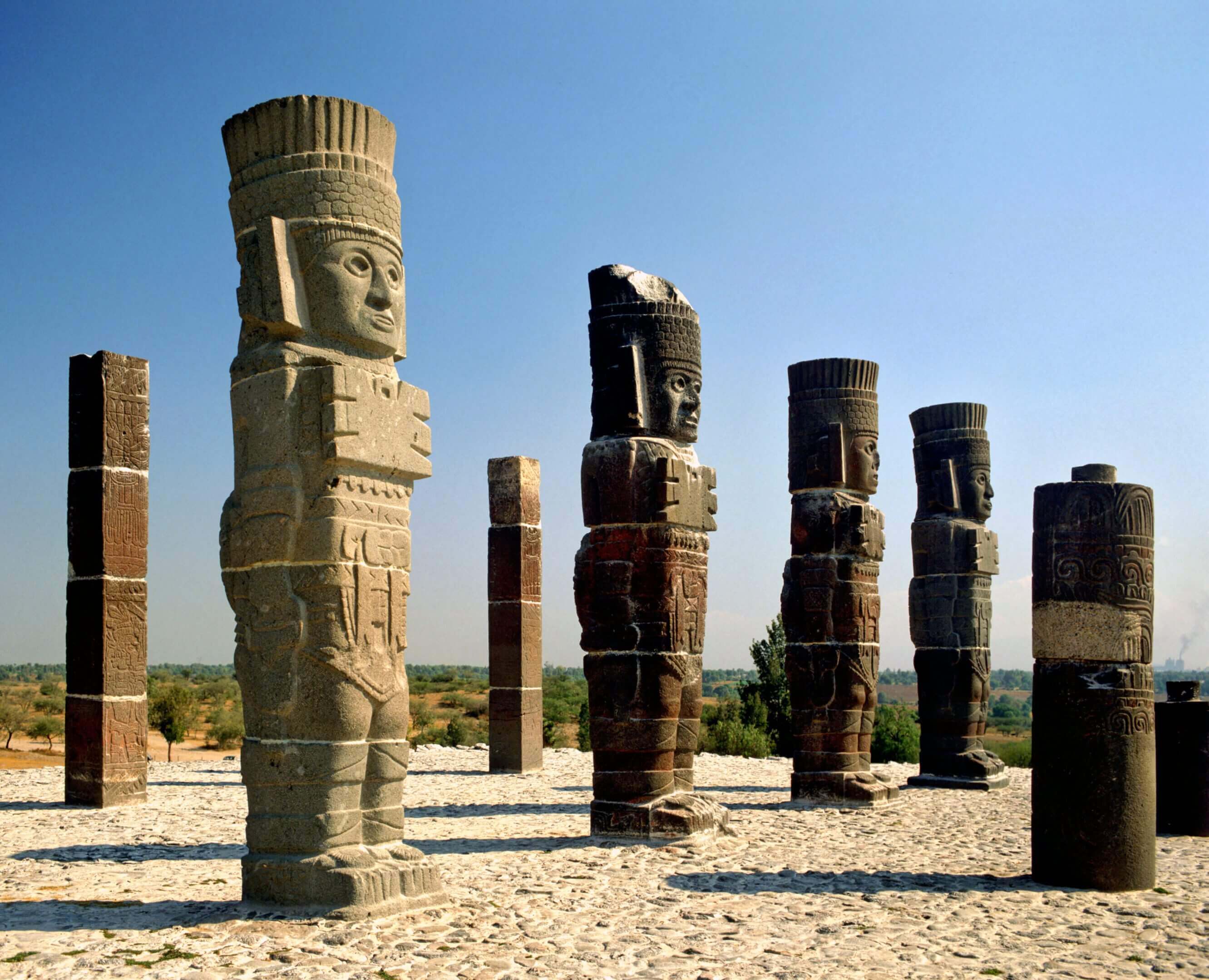 Ancient stone statues and columns under a clear blue sky.